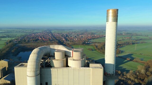 Distant aerial view of the iconic Rugby cement plant chimney against a clear blue sky.