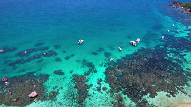 Stunning aerial drone video of Gam Ghi Island on Phu Quoc in south Vietnam with turquoise blue water and vivid coral reefs with tourists snorkeling and jumping off the boats on a hot sunny day