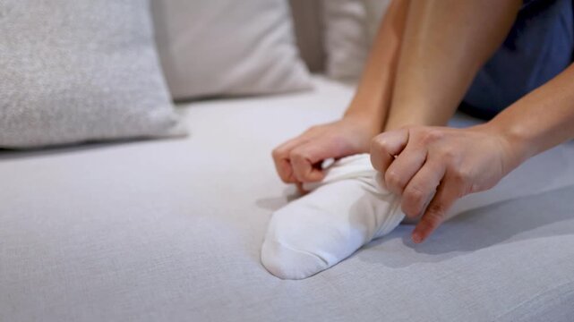 Close Up Of Woman Putting On White Socks While Sitting On Bed