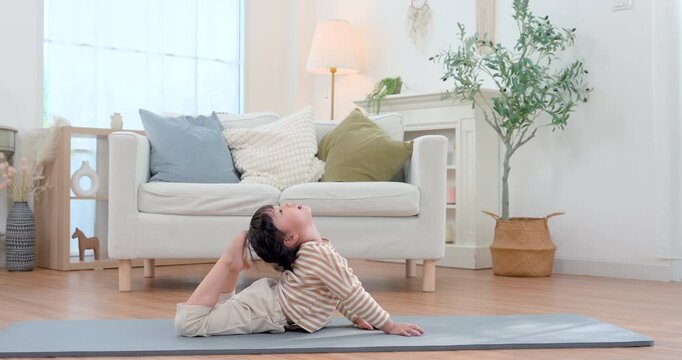 Asian preschool daughter practices flexible backbend pose on yoga mat at home, copying wellness movement from single mother, building body awareness, confidence, coordination, healthy development