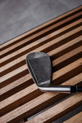 Naklejka premium Close-up of golf iron club head on wooden slatted bench