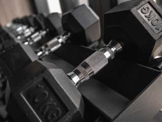 Obraz premium Close-up and row of black hex dumbbells on rack in modern gym