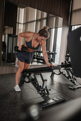Obraz premium Athletic woman performing one arm dumbbell row on bench in modern gym