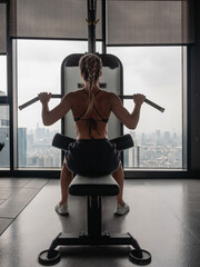 Obraz premium Athletic woman performing lat pulldown exercise on cable machine in modern gym