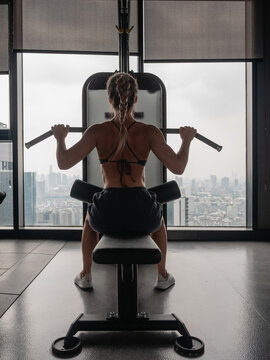 Athletic woman performing lat pulldown exercise on cable machine in modern gym