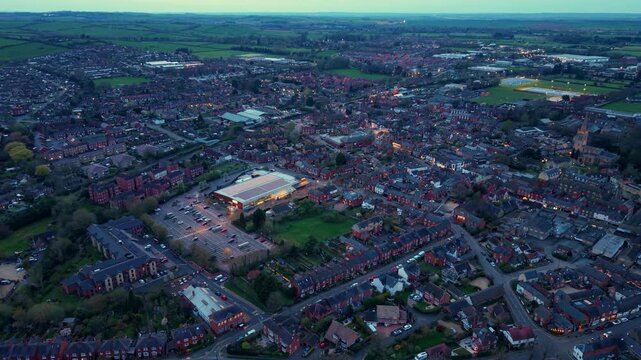 Aerial view of the town of Oakham at twilight with street lights, residential houses, and a large commercial building with a parking lot in Oakham, England, United Kingdom.