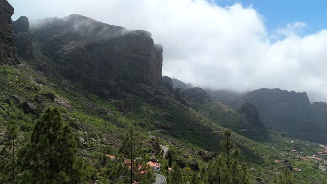 Aerial view of Caminito Roque Nublo with pine trees and rocky cliffs under a misty sky in La Culata, Canarias, Spain.