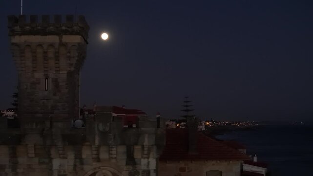 Aerial view of the historic Forte da Cruz stone tower at Tamariz Beach under a full moon at night in Estoril, Lisbon, Portugal.