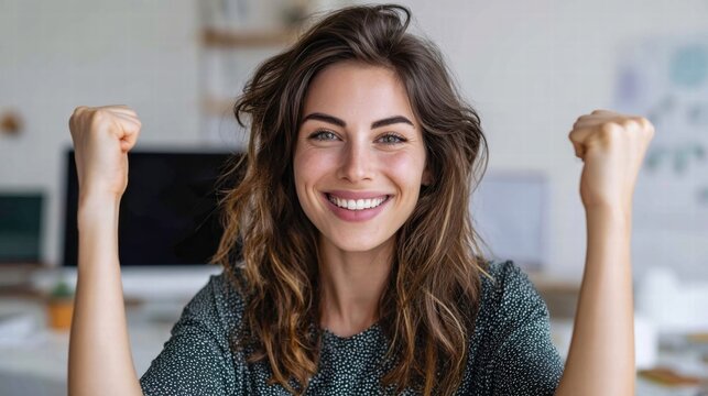 Excited woman celebrating success with raised fists and a beaming smile indoors.