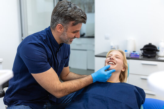Male dentist examining teeth of young blonde female patient. Professional dental checkup, oral hygiene, and healthcare concept. Smiling doctor consulting woman in modern stomatology clinic office.