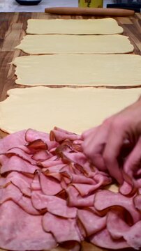 Close-up of a baker's hands placing generous layers of ham and bacon on fresh dough, part of the artisanal production of the iconic Venezuelan Christmas bread.