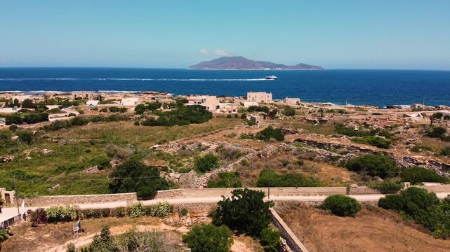 Drone shot tracking a speedboat crossing the Mediterranean off Favignana, Egadi Islands, Sicily. Ancient ruins and coastline in the foreground, Levanzo island on the horizon.