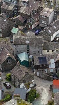 A close vertical orbital aerial shot over the densely packed slate rooftops and winding lanes of Ambleside town centre, Cumbria, showcasing its distinctive stone architecture.