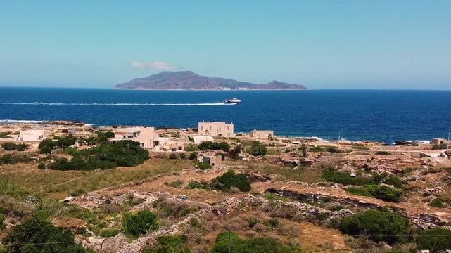 Aerial view of Favignana island, Egadi Islands, Sicily. Ancient stone ruins in the foreground, deep blue Mediterranean sea and Levanzo island on the horizon. A speedboat crosses the frame.