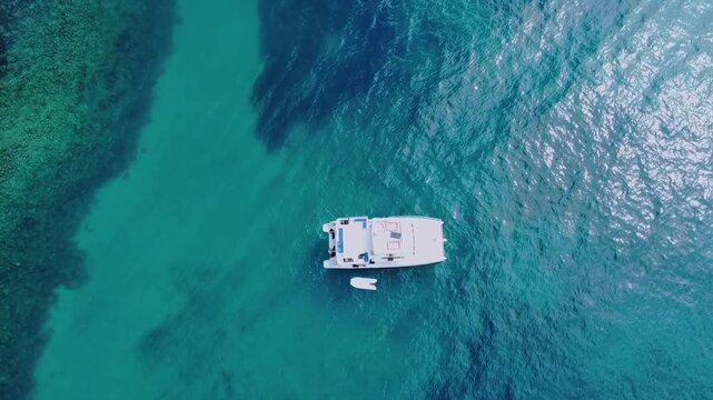 Abrolhos Archipelago near Caravelas Bahia Brazil with motor catamaran anchored above coral reef patches and clear shallow South Atlantic water within marine national park, top down aerial shot