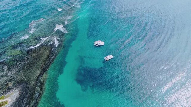 Abrolhos Archipelago near Caravelas Bahia Brazil with shallow coral reef lagoon and darker reef patches in clear South Atlantic water with anchored boats within marine national park, top down slow fly