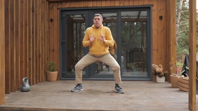 Man performing breathing exercise in squat position on home terrace, controlled respiration training improving body balance outdoors