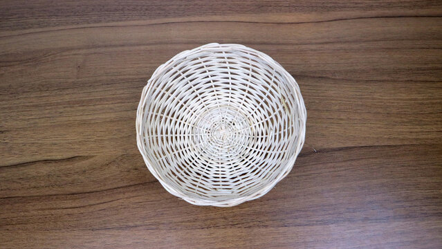 Top down view of an empty white wicker basket centered on a brown wooden tabletop, minimal rustic background