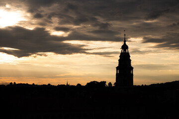 Naklejka premium The castle tower of Cesky Krumlov is visible against a colorful sky during the summer evening. The town shows its historic charm as daylight fades and shadows grow.