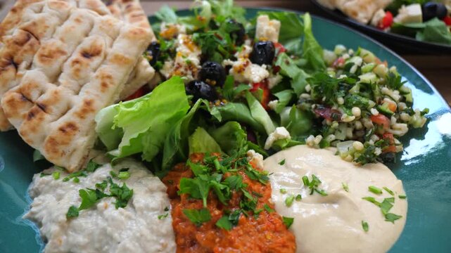 Mediterranean mezze spread with fresh salad topped with feta and olives, pita bread, hummus, baba ghanoush and other dips served on a rustic wooden table for sharing