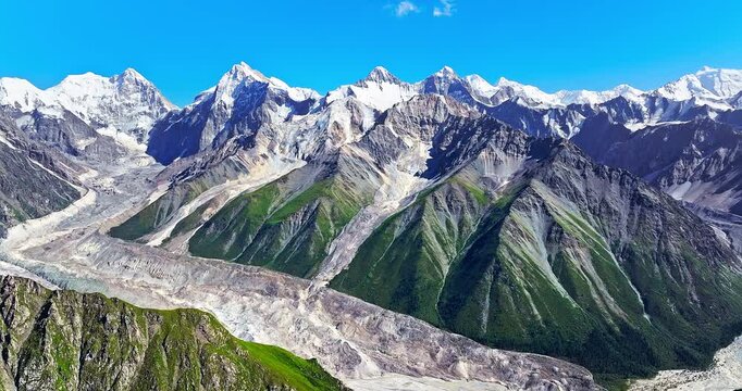 Majestic snow-capped mountain range with green valleys and ancient glaciers under blue sky, Xinjiang, China