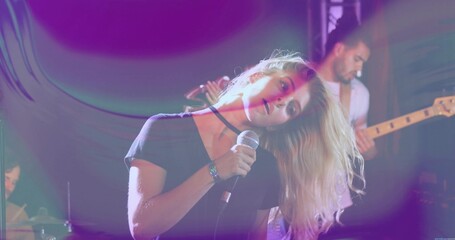 Fototapeta premium Singing lead singer leaning head to side on club stage, holding wired mic, wearing choker