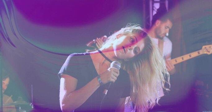 Singing lead singer leaning head to side on club stage, holding wired mic, wearing choker