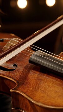 Close-up of a hand using a bow on a violin with blurred background elements, highlighting the intricate details of the instrument and musician's
