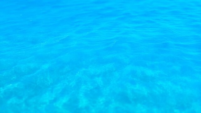Aerial tracking slow motion view of clear turquoise ocean surface with gentle ripples over shallow seabed nearshore tropical waters