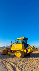 Obraz premium Heavy machinery works on a sandy area with a clear sky and buildings in the background during the day