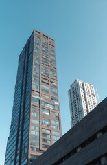 Obraz premium Tall dark skyscraper next to white residential tower under clear blue sky. Modern glass buildings rise high above city streets. Urban architecture cityscape view from below.