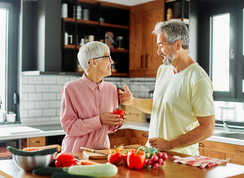 Portrait of happy senior mid aged mature couple prepering meal with fresh vegatebles in kitchen at hpme