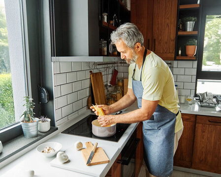 Portrait of happy senior mid aged mature man prepering meal with fresh vegatebles in kitchen at hpme
