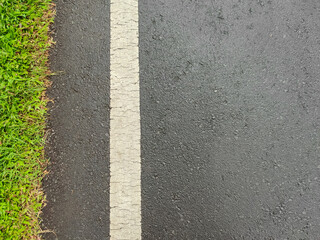 Fototapeta premium Top Down Aerial View of Wet Black Asphalt Road Surface with White Solid Lane Marker Dividing Line and Fresh Green Grass Edge after Rain Texture Background Rural Highway Path Travel Infrastructure