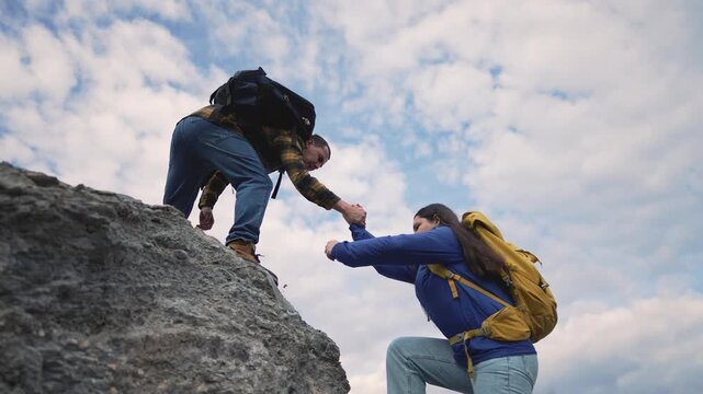 Hiker helping partner climb rocky mountain terrain. Backpackers assist each other while hiking outdoors. Teamwork during climb on rock. Hikers with backpack support partner on mountain adventure.