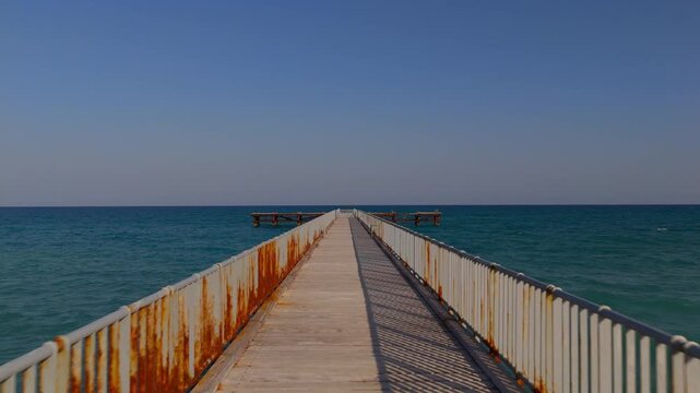 Cinematic Aerial Maneuver Along Wooden Pier Tilting Down to Mediterranean Sea