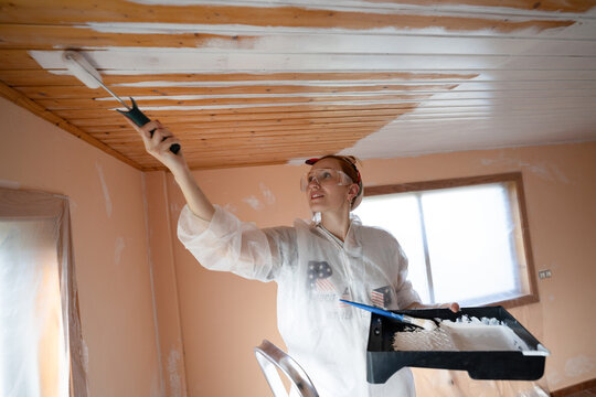 Homeowner painting wooden ceiling white with roller indoors