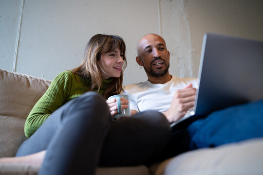 Couple relaxing at home browsing laptop and drinking coffee