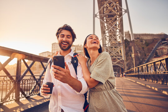 Smiling young man using smart phone with woman at Dom Luis bridge, Porto, Portugal