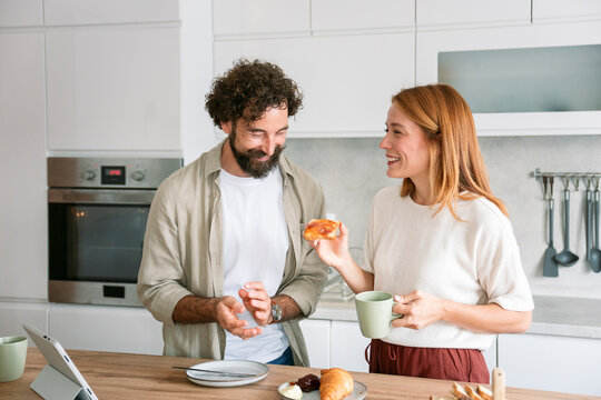 Cheerful couple having breakfast and coffee together in modern kitchen