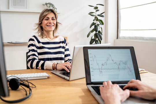Two professionals working on laptops with graphs in an office setting
