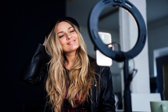 Smiling blond mature influencer vlogging through smart phone on ring light