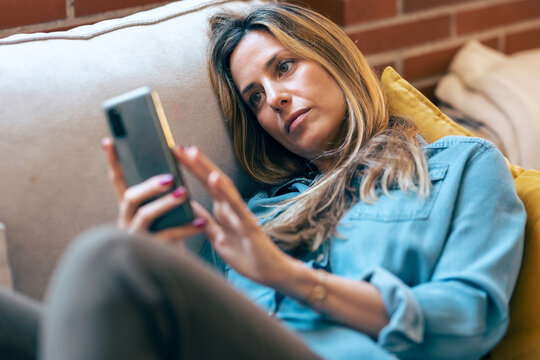 Woman chatting on a smartphone while relaxing on a couch at home