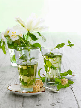 Fresh peppermint tea in a glass with brown sugar on a wooden table