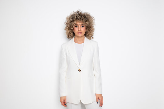Business woman with curly hair in a white blazer looking at the camera in a studio setting