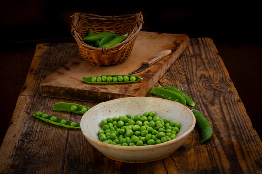 Fresh peas and pods in bowl and wicker basket on rustic wood table