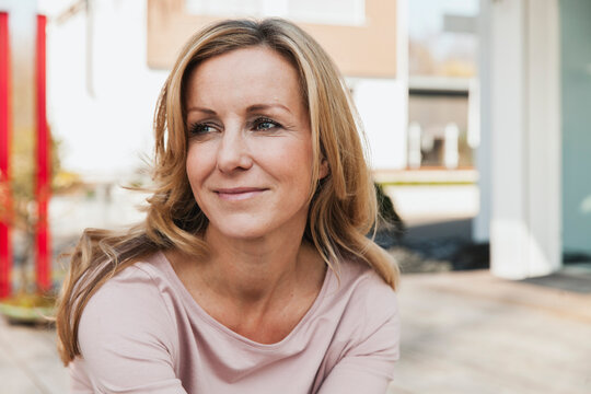 Blonde woman sitting outside house looking away with confident smile