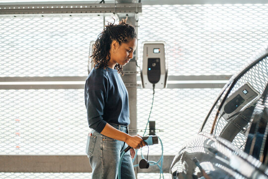 Young businesswoman charging electric car with plug at parking garage