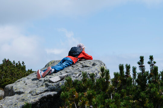 Person relaxing on mountain rock during family adventure in summer