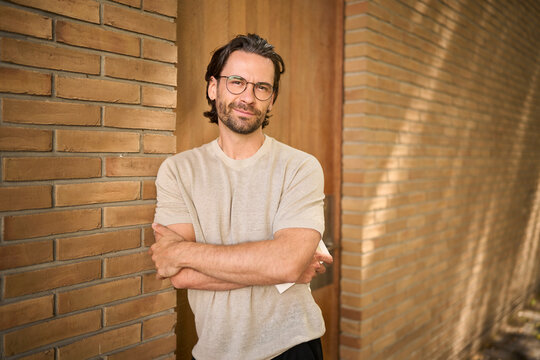 Confident man with glasses standing against brick wall outdoors